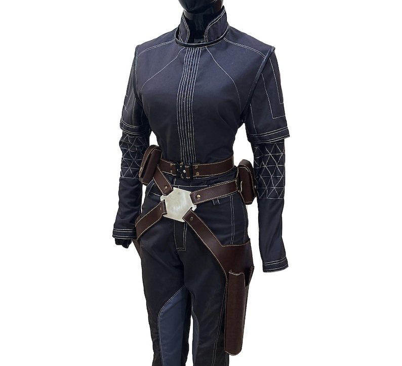 Puede incluir: Un mono azul oscuro con un cintur&oacute;n de cuero marr&oacute;n y una hebilla plateada. El mono tiene una cremallera y un cuello alto. El mono tiene un patr&oacute;n geom&eacute;trico en las mangas.