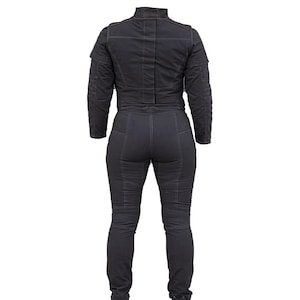 May include: Dark gray denim jumpsuit with a high collar and long sleeves. The jumpsuit features detailed stitching and a fitted silhouette. The back view showcases the design, emphasizing the tailored fit and the overall structure of the garment.