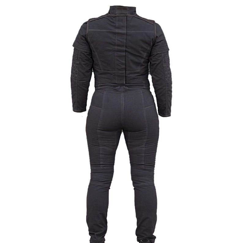 May include: Dark gray denim jumpsuit with a high collar and long sleeves. The jumpsuit features detailed stitching and a fitted silhouette. The back view showcases the design, emphasizing the tailored fit and the overall structure of the garment.