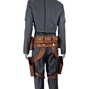 May include: A grey jumpsuit with a matching jacket and brown leather accessories. The outfit includes a belt with pouches, suspenders, and holsters. The jacket has long sleeves and a high collar.