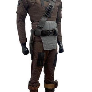 May include: A brown costume with a high collar, shoulder pads, and a utility belt. The outfit includes a chest piece, a shoulder strap with pouches, and matching pants. The boots have brown and tan accents. The mannequin is wearing black gloves.