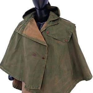 May include: An olive green cape with a hood and brown lining. The cape features two rows of buttons and a classic design. The garment is displayed on a mannequin.