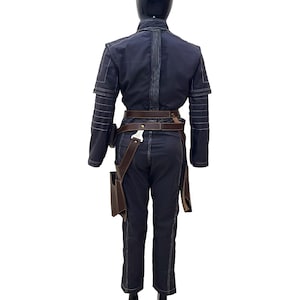 Puede incluir: Un mono azul oscuro con un cintur&oacute;n de cuero marr&oacute;n y una funda en el lado derecho. El mono tiene detalles de costura blanca.