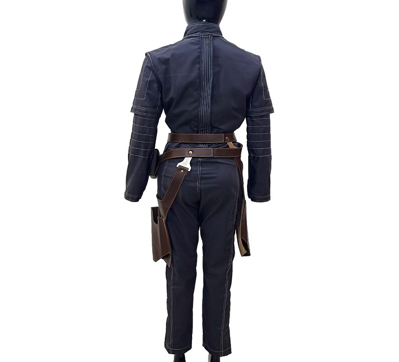 Puede incluir: Un mono azul oscuro con un cintur&oacute;n de cuero marr&oacute;n y una funda en el lado derecho. El mono tiene detalles de costura blanca.