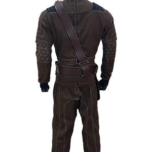 Pu&ograve; includere: Tuta marrone con cuciture bianche, cintura e tracolla abbinate. Il costume presenta dettagli neri sulle spalle e motivi geometrici sulle maniche. Il manichino indossa guanti neri.