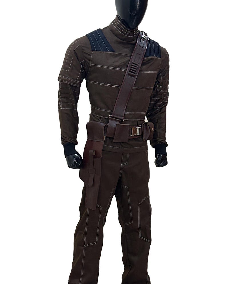 Pu&ograve; includere: Costume marrone con cuciture bianche, con collo alto, dettagli sulle spalle e cintura multiuso con tasche. L'outfit include pantaloni abbinati e una fondina. Il manichino indossa guanti neri.