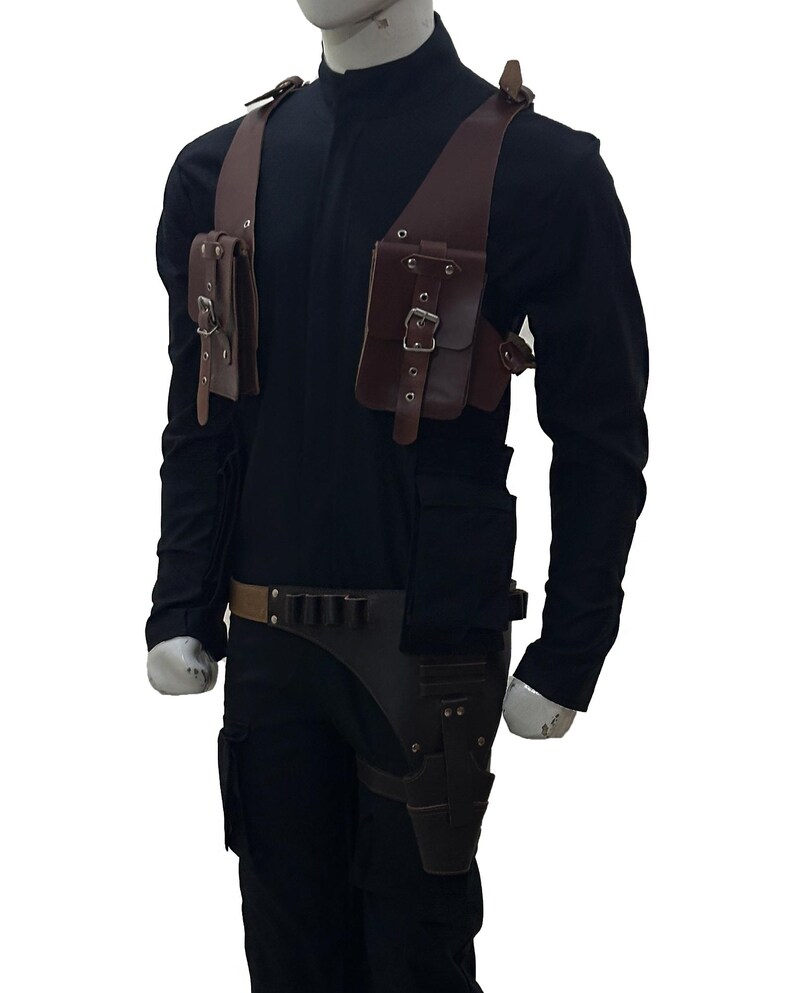 May include: Brown leather shoulder holster with two pouches and a belt with ammunition holders. The holster is worn over a black long-sleeve shirt and pants. The design includes buckles and straps for a secure fit.