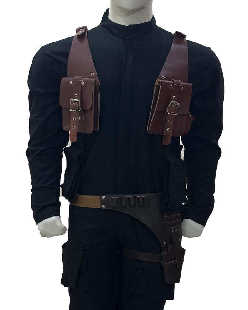 May include: A brown leather tactical harness with two shoulder pouches and a belt with a holster. The harness is worn over a black long-sleeve shirt and pants. The pouches and holster have silver buckles.