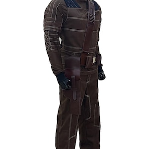 Pu&ograve; includere: Tuta marrone con cuciture bianche, collo alto e tracolla e fondina in pelle marrone scuro. L'outfit include guanti neri e una copertura per il viso nera. Il design suggerisce un tema tattico o futuristico.