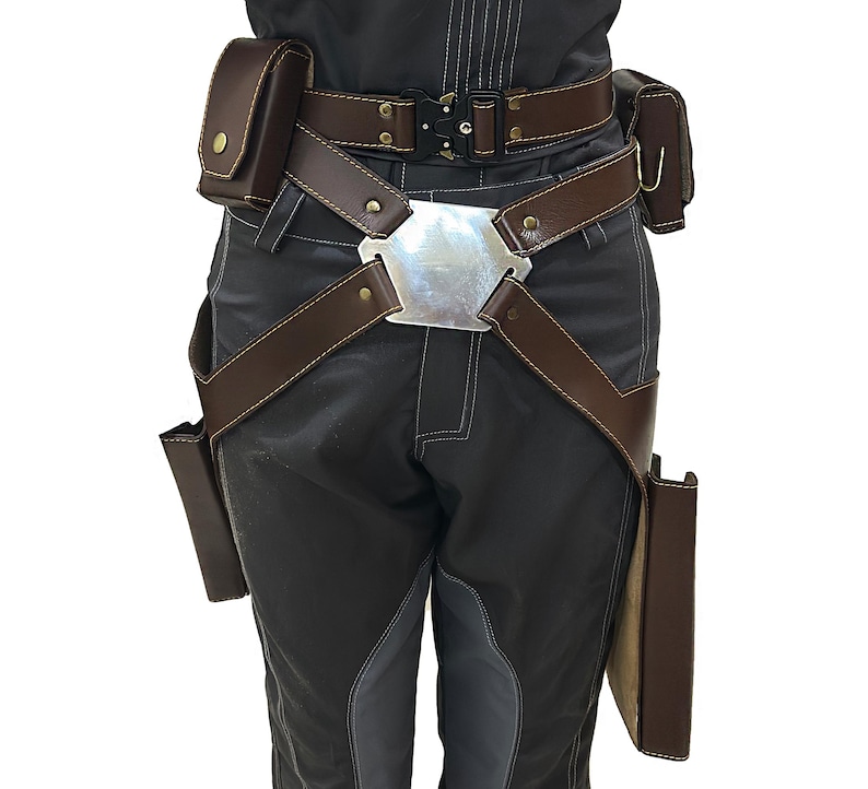 Puede incluir: Un cintur&oacute;n de cuero marr&oacute;n con una hebilla plateada y m&uacute;ltiples bolsas. El cintur&oacute;n se lleva sobre pantalones grises oscuros.