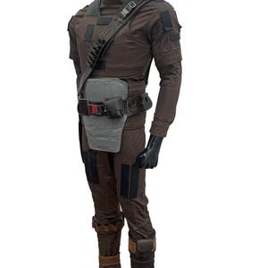 May include: Brown tactical jumpsuit with a high collar, shoulder strap, and multiple pockets. The outfit includes a gray chest plate, a black belt with pouches, and brown boots with tan accents. The mannequin is wearing black gloves.