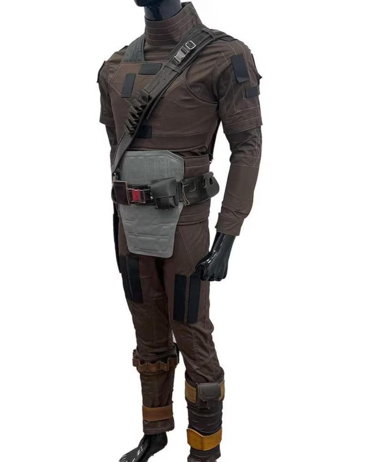 May include: Brown tactical jumpsuit with a high collar, shoulder strap, and multiple pockets. The outfit includes a gray chest plate, a black belt with pouches, and brown boots with tan accents. The mannequin is wearing black gloves.