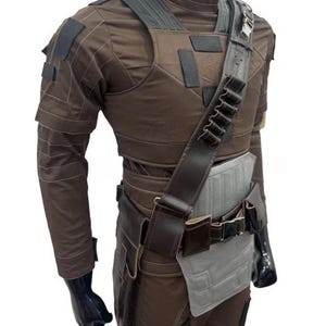 May include: A brown costume with a high collar, shoulder straps, and a utility belt. The outfit includes a chest piece, long sleeves, and a holster. The costume has black accents and a gray panel on the waist.