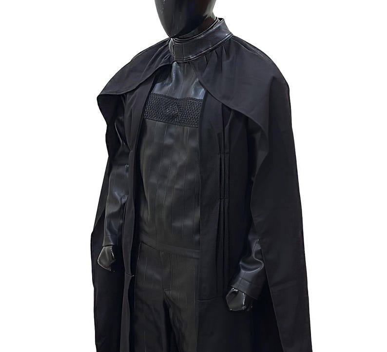 May include: A black costume with a long black cape. The costume has a high collar and a textured design on the chest.