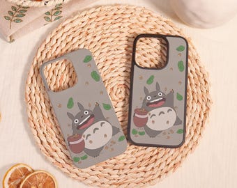May include: Two grey smartphone cases featuring a cartoon character with large ears, a white belly with chevron markings, and a brown pot. The design includes scattered green leaves and small brown acorns across the grey background.