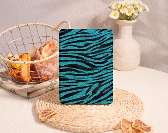 May include: A rectangular electronic reader cover featuring a vibrant teal and black zebra stripe pattern with a glittery, textured finish. The cover stands upright on a woven circular mat, displaying a bold animal print design.