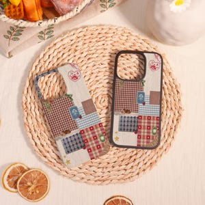 May include: Two phone cases with a patchwork design. The cases feature a mix of patterns including gingham, floral, and solid colors in red, blue, and brown. Each case has a heart-shaped design at the top.