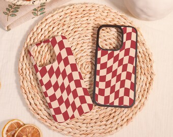 May include: Two phone cases with a checkered pattern. The cases are red and white with a black border. The cases are sitting on a woven straw surface.