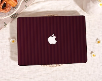May include: A burgundy laptop featuring vertical stripes and a white Apple logo. The laptop sits on a woven mat. A basket of food and a vase of flowers are in the background. The image suggests a tech and lifestyle theme.