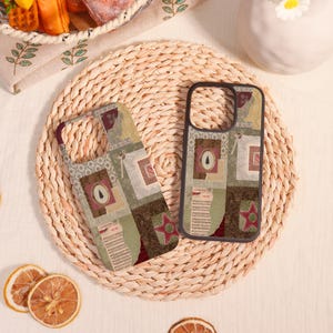 May include: Two phone cases with a patchwork design featuring a Christmas tree, star, and sheet music elements. The cases have a mix of green, brown, and red tones. They rest on a woven straw mat.