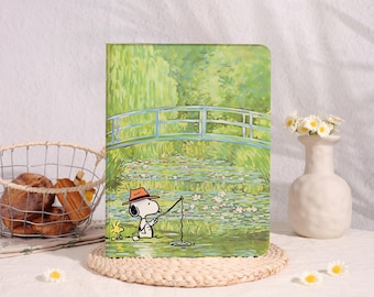 May include: A rectangular tablet case featuring a printed illustration of Snoopy wearing an orange hat and fishing in a pond with water lilies, set against a background of a green garden with a blue bridge, reminiscent of an impressionist painting.