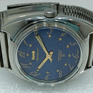 May include: A silver wristwatch with a blue face and gold accents. The watch face has the text "Kohinoor" and "Para Shock 17 Jewels".