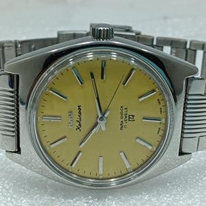 May include: A silver Kohinoor wristwatch with a gold-coloured face and a matching silver band. The watch face displays the brand name, the words "Para Shock 17 Jewels", and the number 17. The watch has a classic, retro design.