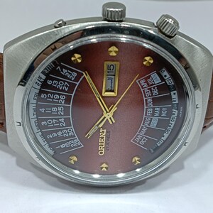 May include: A vintage Orient 21 Jewels wristwatch with a brown dial and calendar features. The watch has a stainless steel case, gold-tone hands and markers, and a brown leather strap. The dial displays the date and month, with Arabic numerals.
