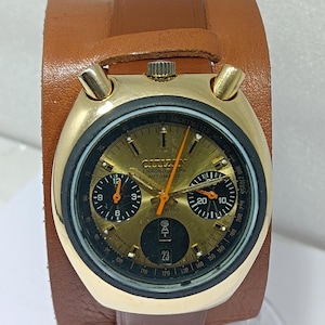 May include: Vintage gold-toned Citizen chronograph watch with a brown leather cuff. The watch face features black sub-dials, orange hands, and the date. The watch has the text "Citizen Chronograph Automatic 23 Jewels".