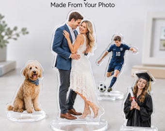 May include: Custom acrylic standees featuring printed photographs of a golden doodle, a couple embracing, a soccer player in action, and a graduate in a cap and gown. Each clear acrylic cutout is mounted on a circular base for display purposes.