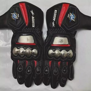 Pode incluir: Um par de luvas de moto pretas com detalhes vermelhos e prateados. As luvas exibem o logotipo "MV AGUSTA" e são projetadas para proteção. Possuem proteção acolchoada nas articulações e são feitas de couro.