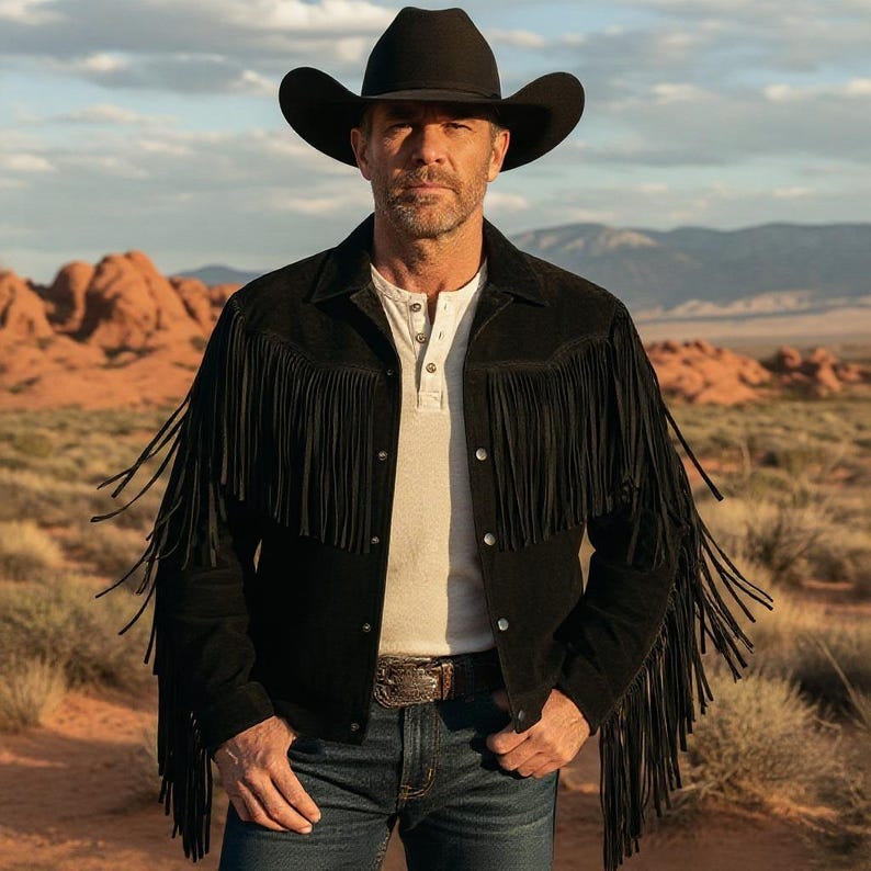 May include: A black suede fringe jacket with a black cowboy hat and a white Henley shirt. The jacket has long fringe detailing across the chest and sleeves. The person is wearing blue jeans and a decorative belt buckle.