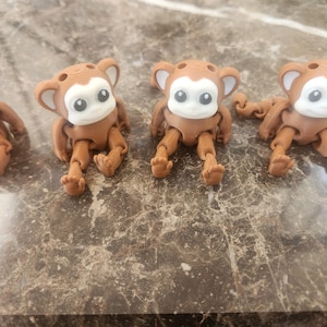 May include: Four brown articulated monkey toys with white eyes and a brown body. The monkeys are posed in a sitting position with their arms and legs outstretched.