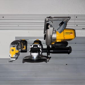 May include: A collection of power tools, including a yellow and black circular saw, a grinder, and a reciprocating saw. The tools are mounted on a gray track system against a white wall.