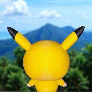 May include: A yellow Pikachu figure with black-tipped ears and small pink hands and feet. The figure is set against a backdrop of a mountain, blue sky, and green foliage. The figure is a popular character from the Pok&eacute;mon franchise.