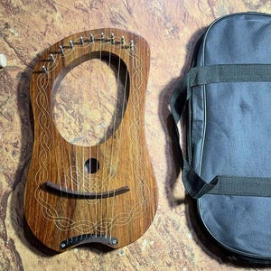 May include: A wooden lyre with a decorative Celtic knot design, a tuning wrench, and two strings. The lyre is in a black carrying case.