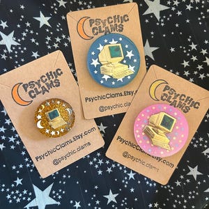 May include: Three round pinback buttons with computer designs on a black background with white stars. The buttons are on brown cardstock with the text "PSYCHIC CLAMS" and Etsy and social media information.