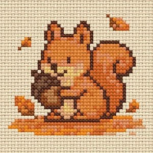 Può includere: Motivo a punto croce di uno scoiattolo che tiene una noce, nelle tonalità dell'arancione e del marrone. Lo scoiattolo è seduto su un letto di foglie, con altre foglie sparse. Lo sfondo è un tessuto beige.