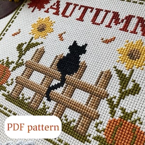 Könnte beinhalten: Kreuzstichmuster mit dem Wort "HERBST" in Rot, einer schwarzen Katze auf einem braunen Zaun, Sonnenblumen, Kürbissen und fallenden Blättern. Das Design befindet sich auf weißem Stoff mit einem grünen Rand. Der Text "PDF pattern" ist ebenfalls enthalten.