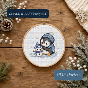 May include: A cross-stitch project in a round wooden embroidery hoop featuring a penguin and a small snowman wearing blue hats and scarves on a white fabric background. The text SMALL & EASY PROJECT and PDF Pattern appear in blue boxes.