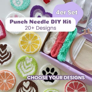 Könnte beinhalten: Ein Punch-Needle-DIY-Set mit einer Box, die weißes, korallenfarbenes und mintgrünes Garn, einen hölzernen Stickrahmen und Stoff enthält. Um die Box herum liegen verschiedene runde Punch-Needle-Untersetzer mit Motiven wie Zitrusfrüchten und Pfoten.