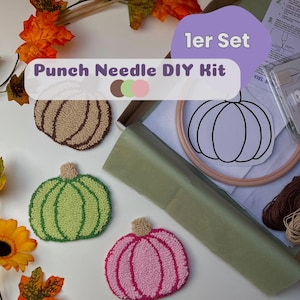 Könnte beinhalten: Ein Punch-Needle-DIY-Set bestehend aus einem Karton mit einem hölzernen Stickrahmen, weißem Stoff mit Kürbis-Umriss und Garn. Drei fertige Kürbis-Untersetzer in Beige, Hellgrün und Rosa sind daneben abgebildet.