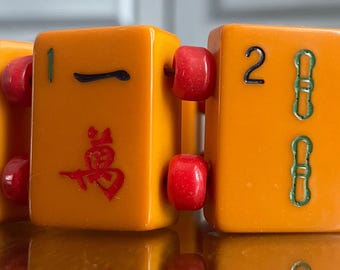 Puede incluir: Un brazalete hecho de fichas de mahjong de plástico naranja y rojo. Las fichas tienen caracteres chinos y números.