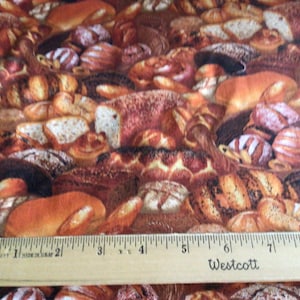May include: A close-up of a fabric with a pattern of various breads and pastries. The fabric is brown, tan, and white. A wooden ruler with the text "Westcott" is placed on top of the fabric.