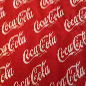 May include: Red fabric with a repeating pattern of the Coca-Cola logo in white script. The logo is slightly blurred, creating a sense of movement across the surface. The background is a solid, vibrant red.