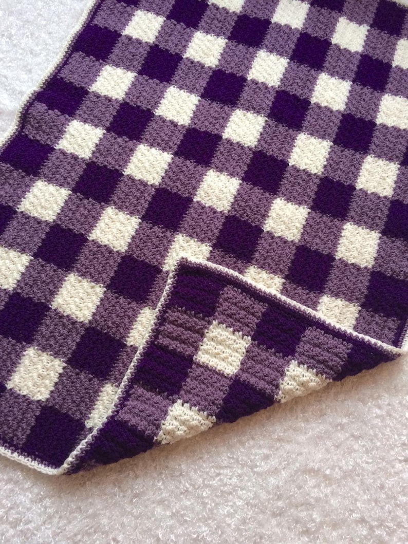 May include: Purple and white checkered crochet blanket with a soft, fuzzy texture.
