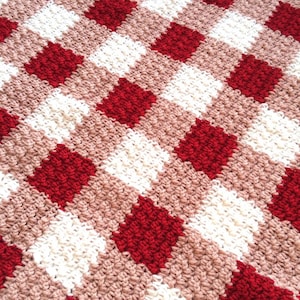 May include: A red and white checkered crochet blanket with a pink background. The blanket is made with a soft, textured yarn.
