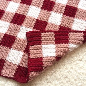 May include: A red, white, and pink crocheted blanket with a gingham pattern.
