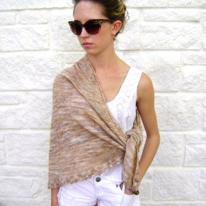 May include: A woman wearing white shorts and a white tank top with a brown and beige knitted shawl draped over her shoulders. She is wearing brown cat-eye sunglasses.