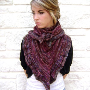 May include: A woman wearing a dark purple and brown shawl with a black jacket and blue denim shorts.